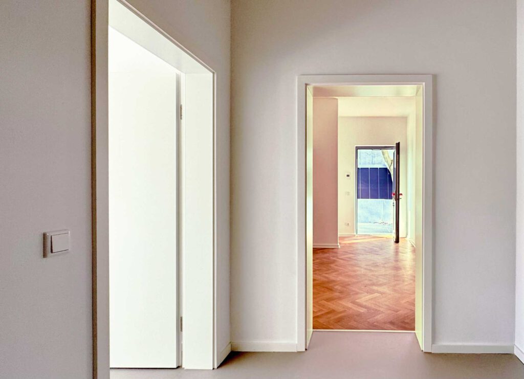 ein Flur mit zwei offenen Türen, eine mit Blick auf ein tolles Zimmer mit Parkett mit einer weiteren offenen Tür in den Hof